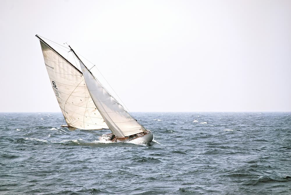 Velero clásico escorado navegando contra las olas y enfrentándose al viento de poniente en el mar.