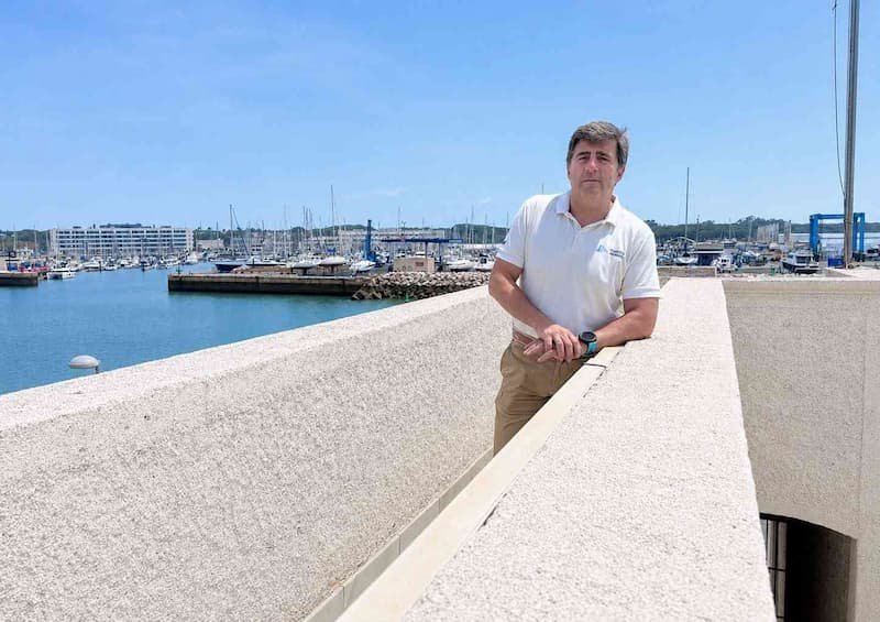 Nicolás Figueras leaning on a white stone wall with the Puerto Sherry marina and moored boats in the background on a sunny day.